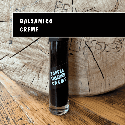 Schmale Glasflasche mit dunkler Kaffee-Balsamicocreme vor rustikalem Holz, Feinkost aus Nidda.