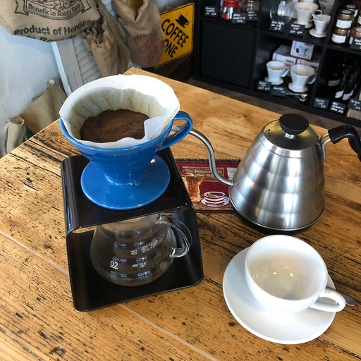Filterkaffee im Handfilter mit Kaffeekanne und Schwanenhalskessel auf Holztisch.